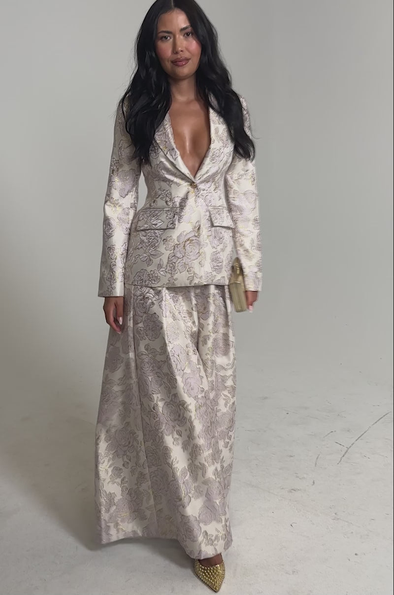 Video of woman modeling the CHERI BROCADE BLAZER, featuring a waist-defining fit and deep neckline. She holds a small gold clutch, smiling softly against a neutral background.