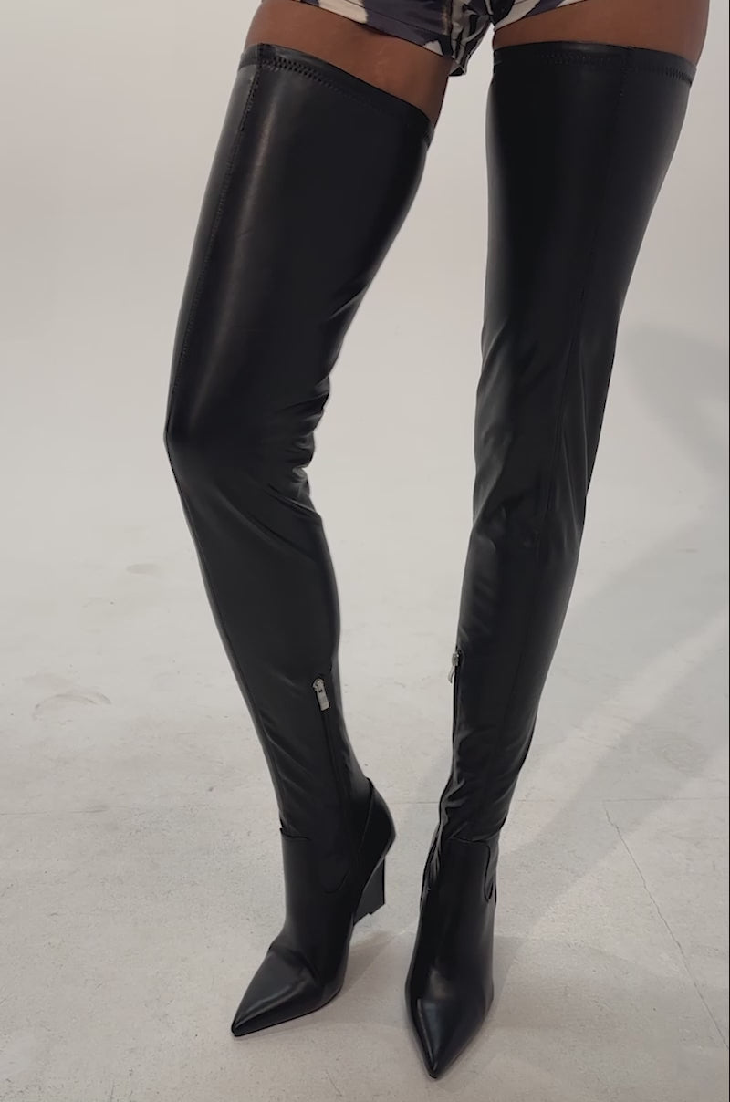Video of a woman modeling the striking AZALEA WANG VIREX BLACK PU WEDGE STRETCH BOOTS, which feature a sleek thigh-high silhouette and zipper detailing.