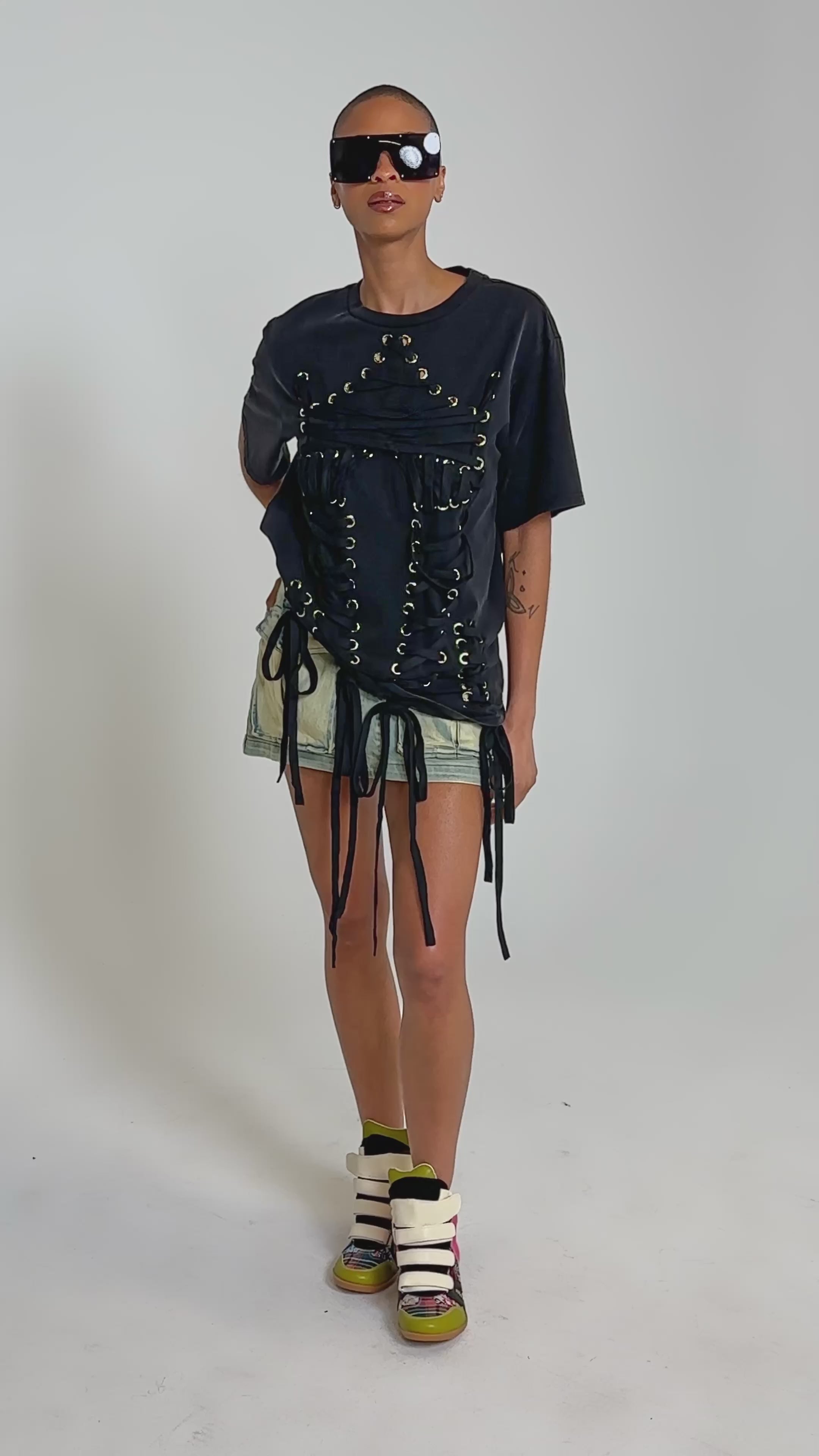 Video of woman modeling the LACED UP MINERAL WASH T-SHIRT with hanging ties, and light skirt, confidently standing against a plain background—a bold concert look.