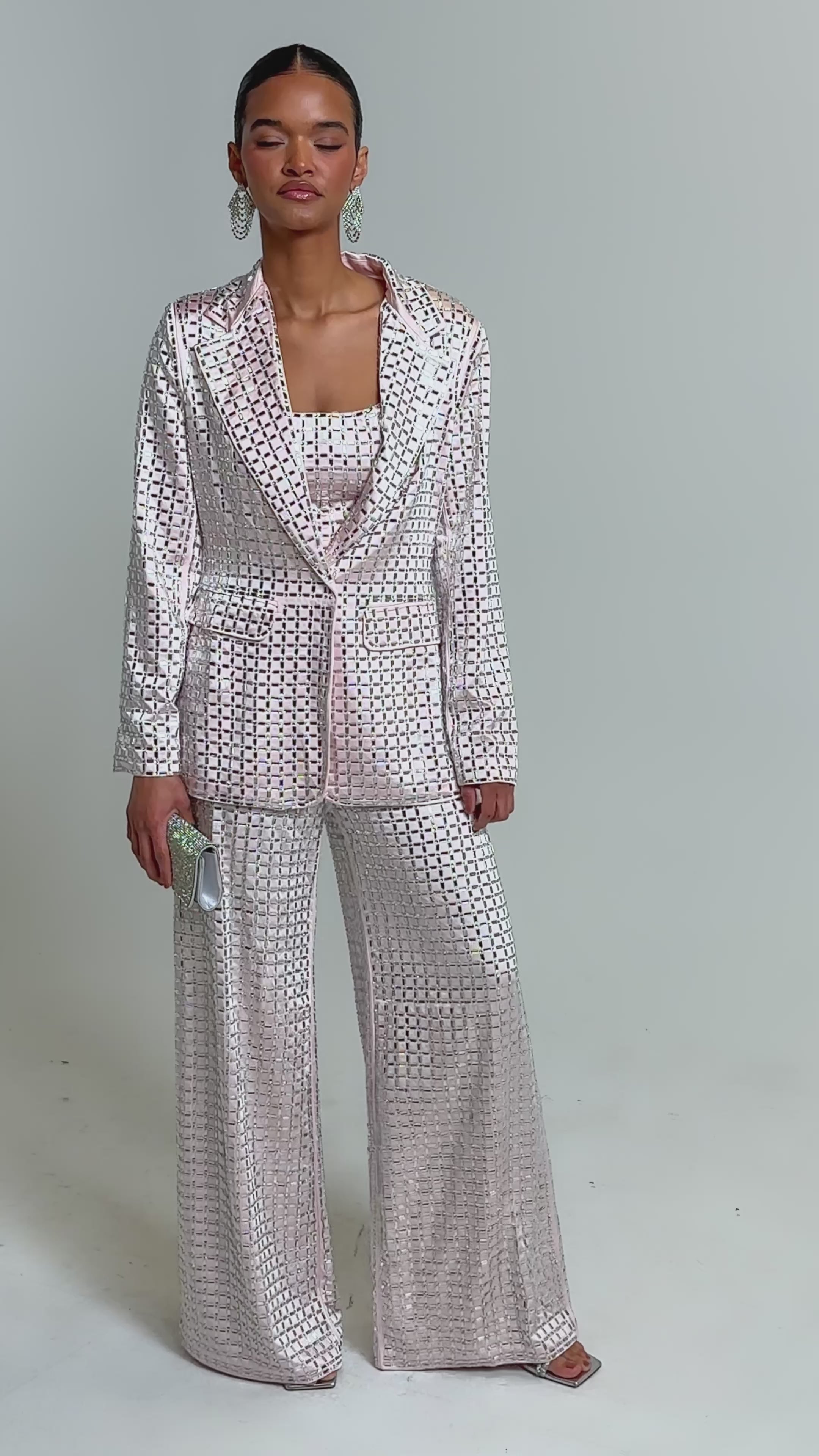 Video of woman modeling the LILA EMBELLISHED SATIN BLAZER IN LIGHT PINK with rhinestone details and a deep neckline, styled with matching square-patterned pants and statement earrings.