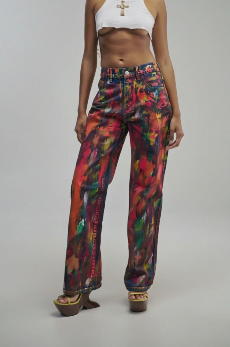Video of a woman modeling the THOUGHTS ALL OVER THE PLACE PAINTED DENIM—wide-leg jeans featuring a vibrant, multicolor abstract paint splatter pattern.