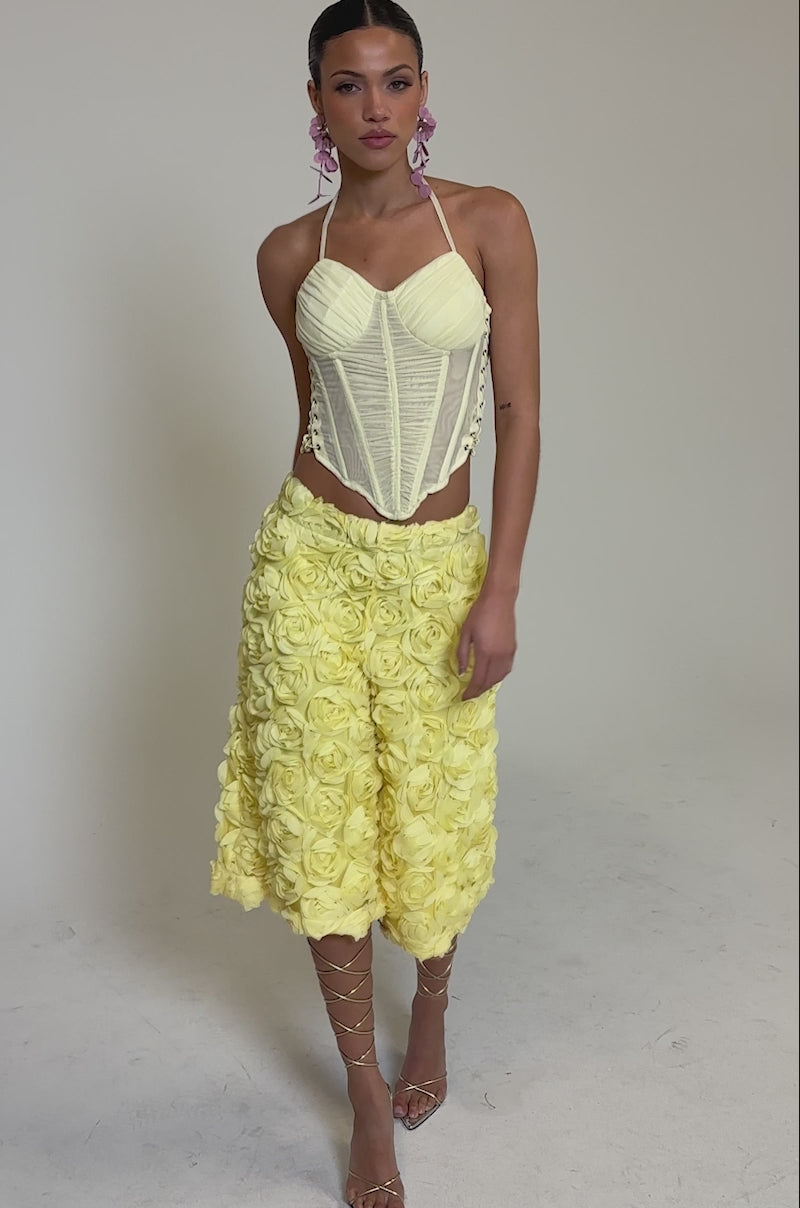Video of woman modeling the ROSE PETAL BERMUDA SHORTS decorated with large fabric roses, paired with strappy high-heeled sandals.