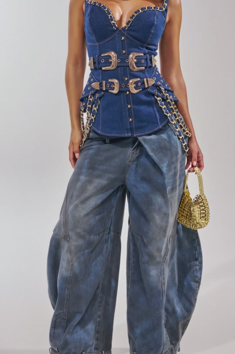Video of woman modeling the WHAT IN TARNATION DENIM CORSET, featuring gold chains and buckles, with denim jeans. 