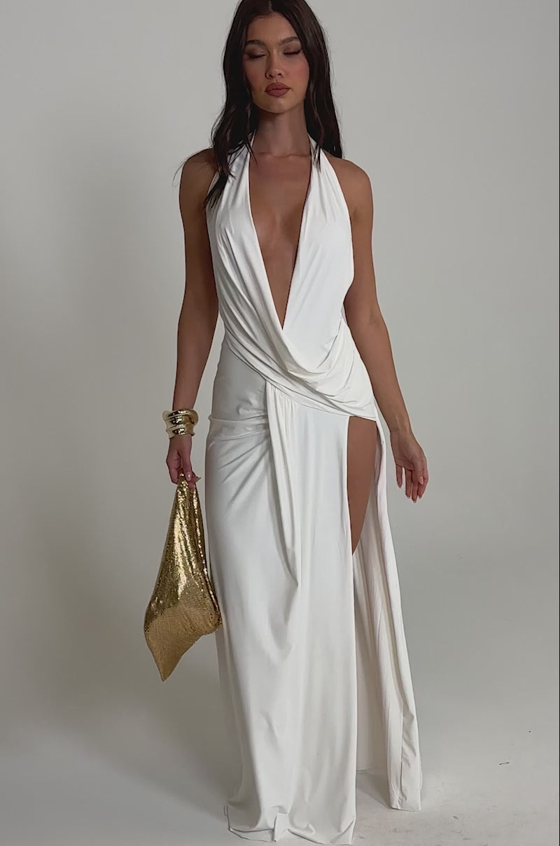 A video of a woman in the HEAD TURNING HALTER MAXI DRESS IN WHITE, a sleeveless deep V-neck maxi with a high slit. 