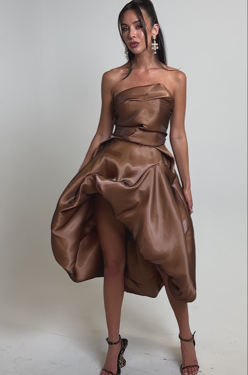 A video of a woman in the HEAD OVER HEELS HIGH-LOW DRESS, a strapless tulle cocktail dress in shiny brown-burgundy with a voluminous skirt. 