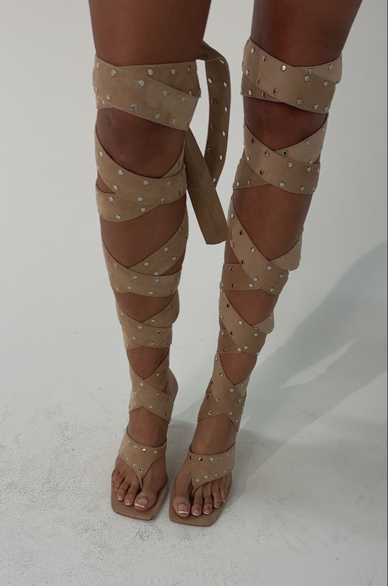 Video of woman modeling the AZALEA WANG SODALITE NUDE FAUX SUEDE LACE UP SANDAL, featuring nude faux suede, lace-up design with silver studs, a square toe heel, and straps wrapping up to just below the knees.
