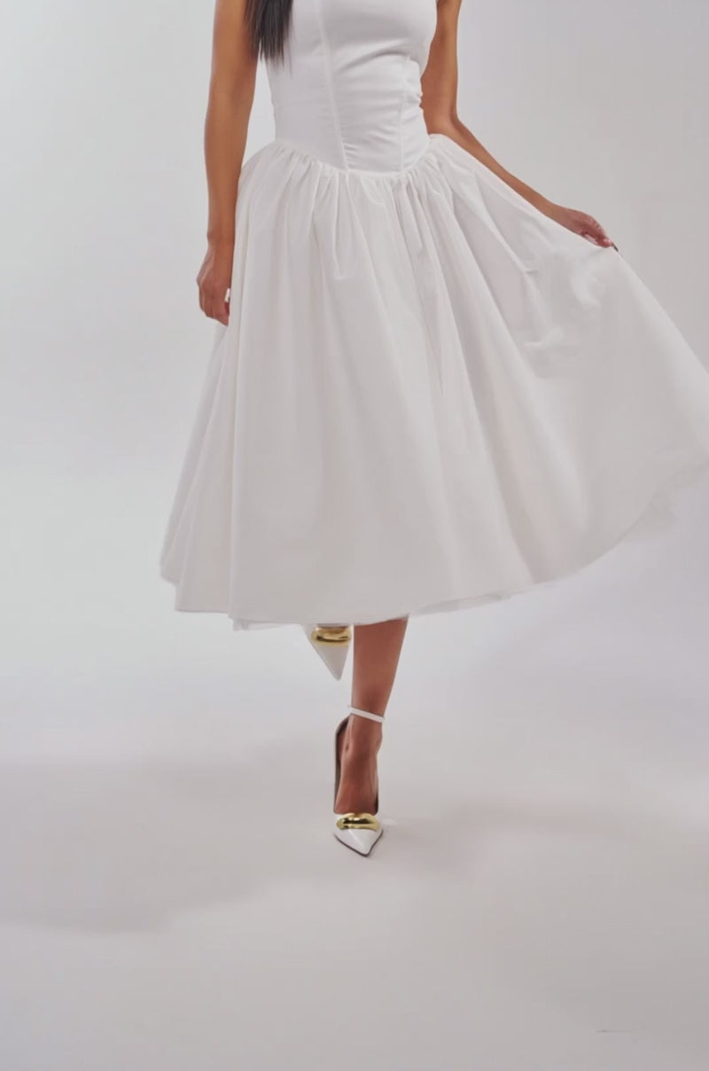 A video of a woman in the SUNDAY AFTERNOON POPLIN MIDI DRESS IN WHITE wearing pointed white heels, and posing against a plain light background.