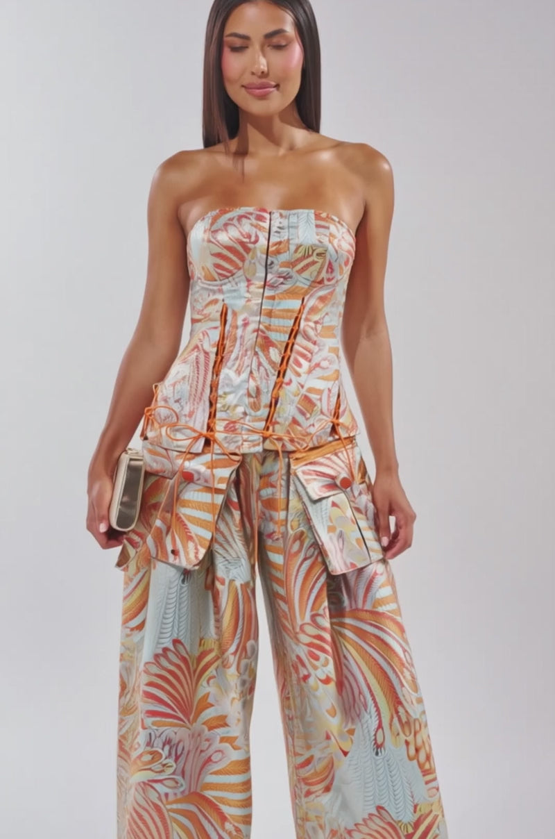 A video of a woman wearing the MARTHA FLORAL CORSET, a strapless metallic brocade top with an ornate orange and silver floral pattern, paired with wide-leg pants.