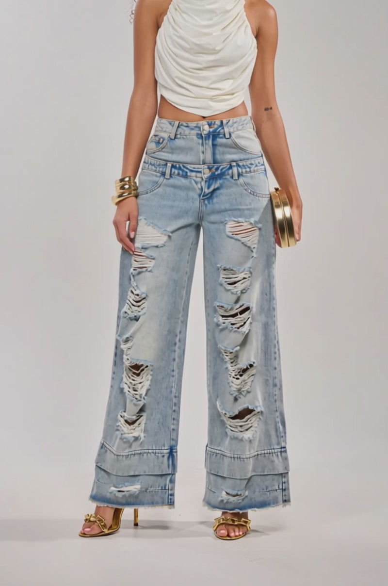 Video of woman modeling the GO GET SOME DOUBLE WAISTED DENIM, gold heeled sandals, a white top, gold bracelets, and holding a small round gold handbag.