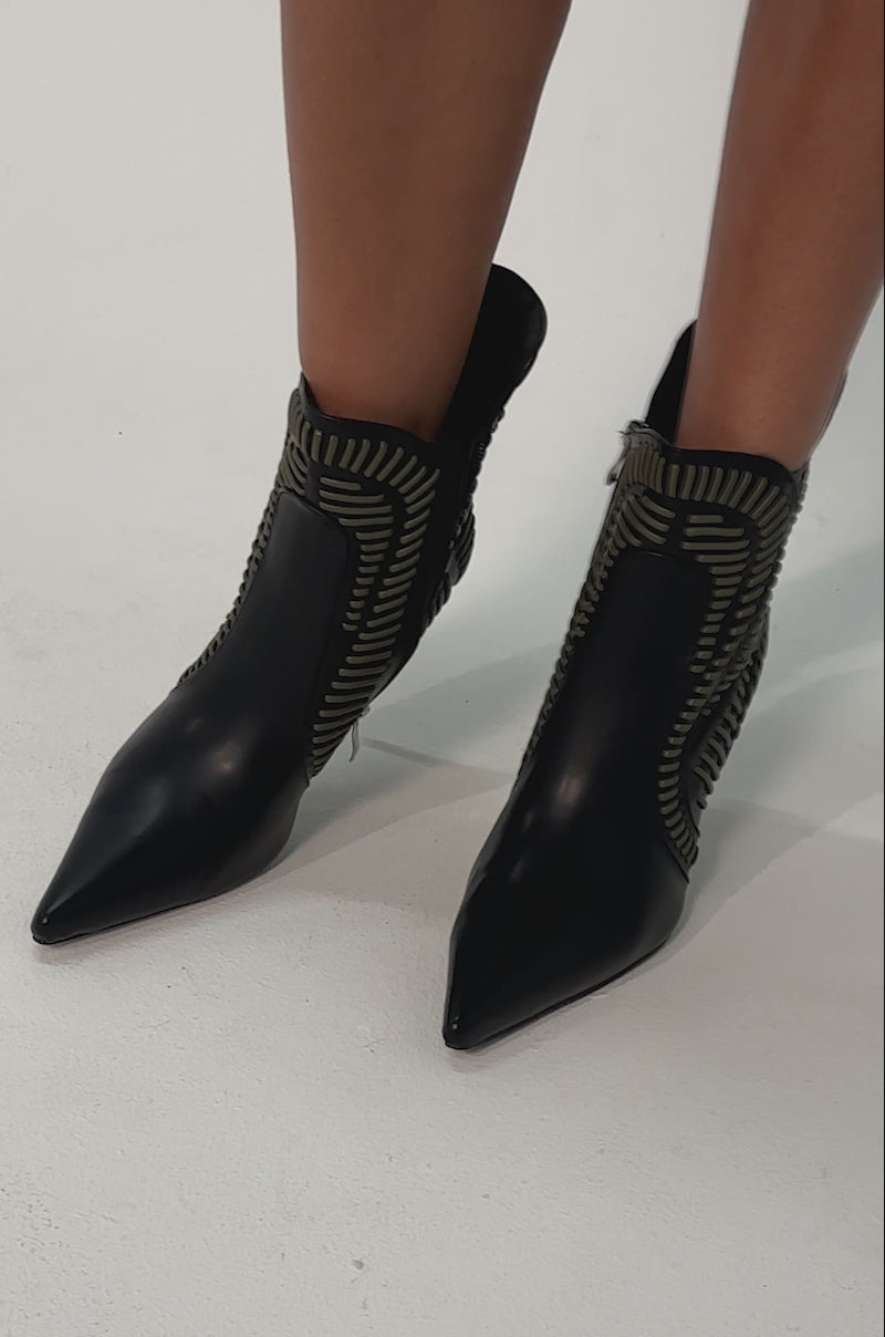 Video of woman modeling the AKIRA GOLD WEAVER BLACK AND OLIVE BOOTIE—black ankle boots with a pointed toe and intricate gold details.