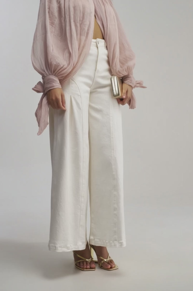 Video of woman modeling the SOFT SEDUCTION CHIFFON BLOUSE—a light pink mock neck top with billowy sleeves—paired with matching high-waisted pleated pants, posing confidently indoors in soft lighting.