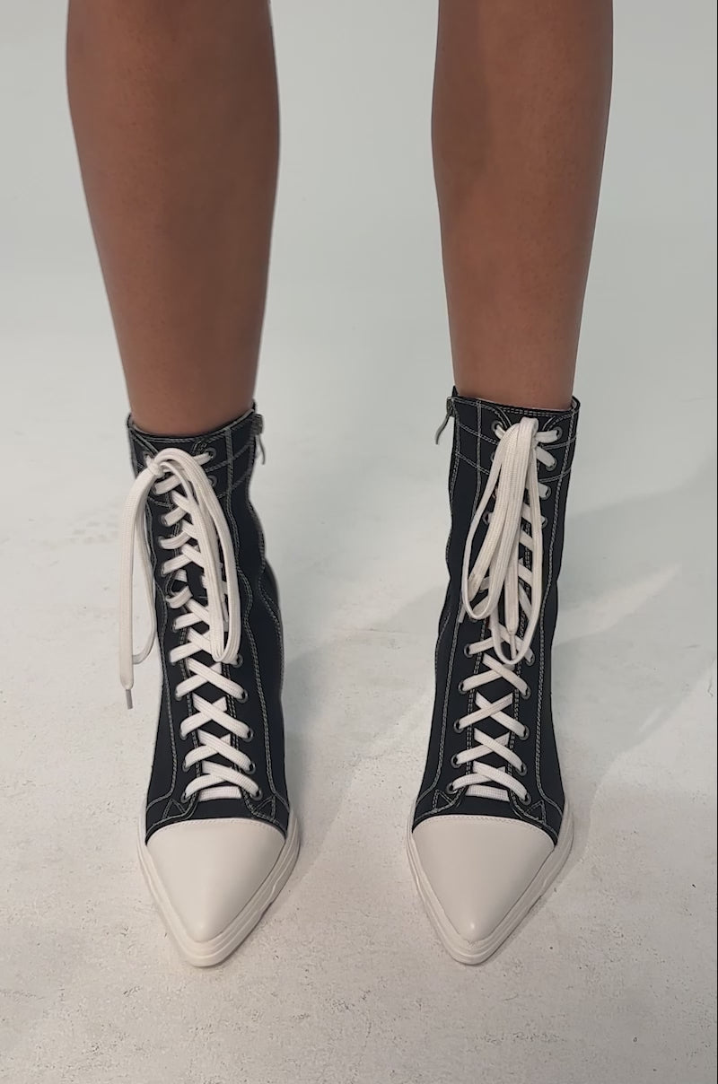 A video of a model wearing the AZALEA WANG COSIMA BLACK BLOCK SNEAKER HEEL. It is a high-top black denim ankle boot with white stitching, laces, and a white block heel.