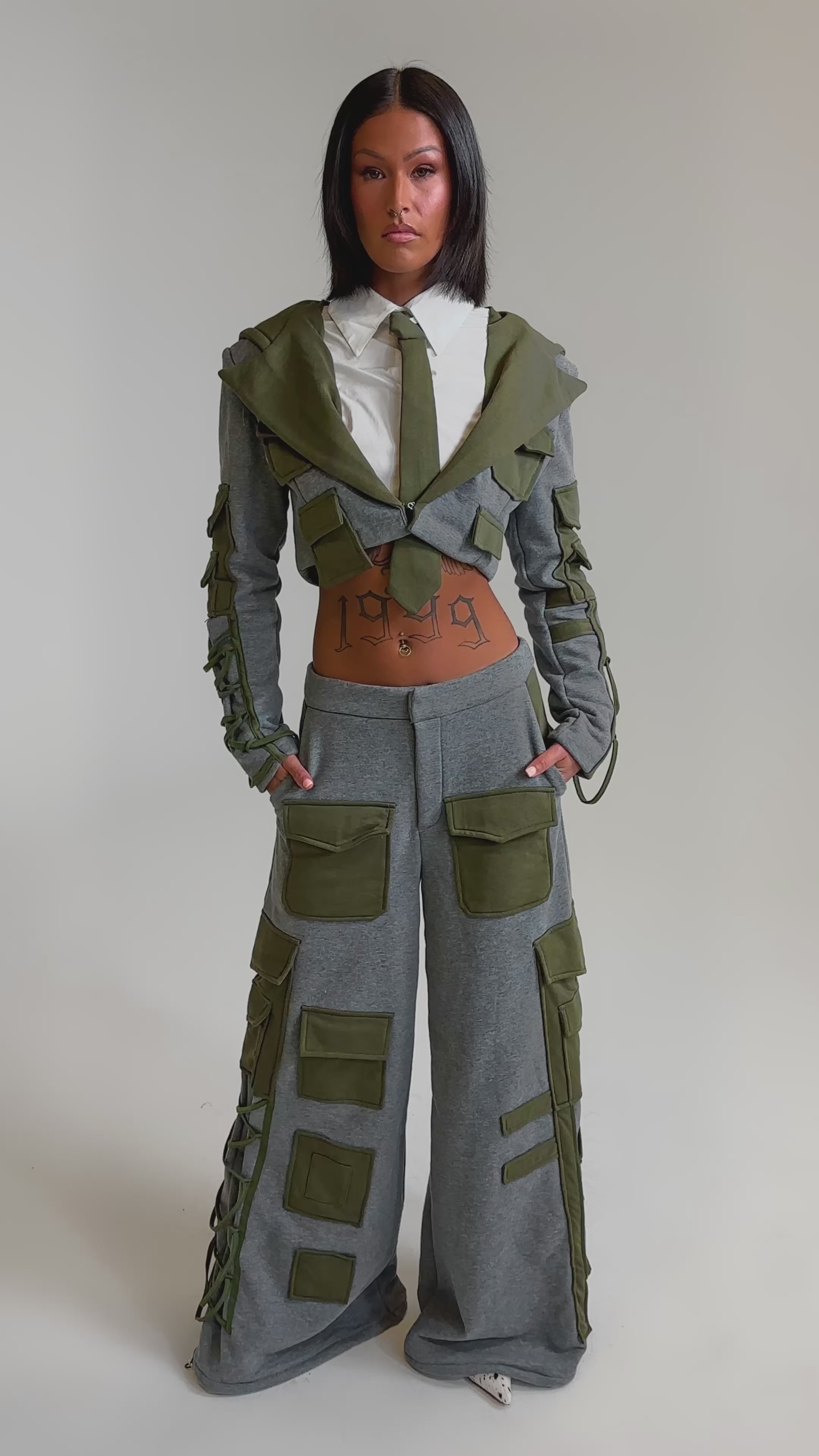 A video of a woman in the CRAZY IN LOVE TROUSER, a gray wide-leg pant paired with a matching cropped jacket featuring olive green patches. 