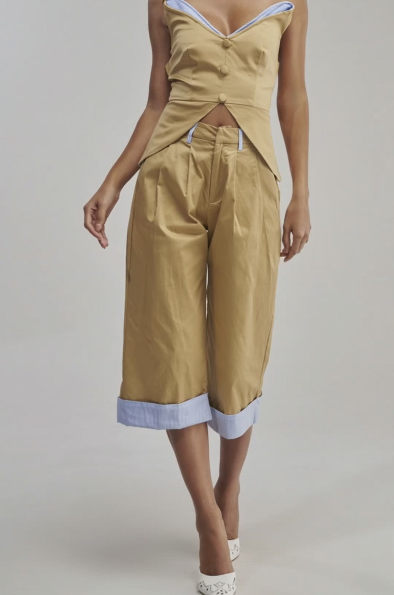A video of a woman in the TOP TIER POPLIN TRIM PANT, tan culottes with light blue striped poplin trim, styled with an off-the-shoulder top and white pointed heels.