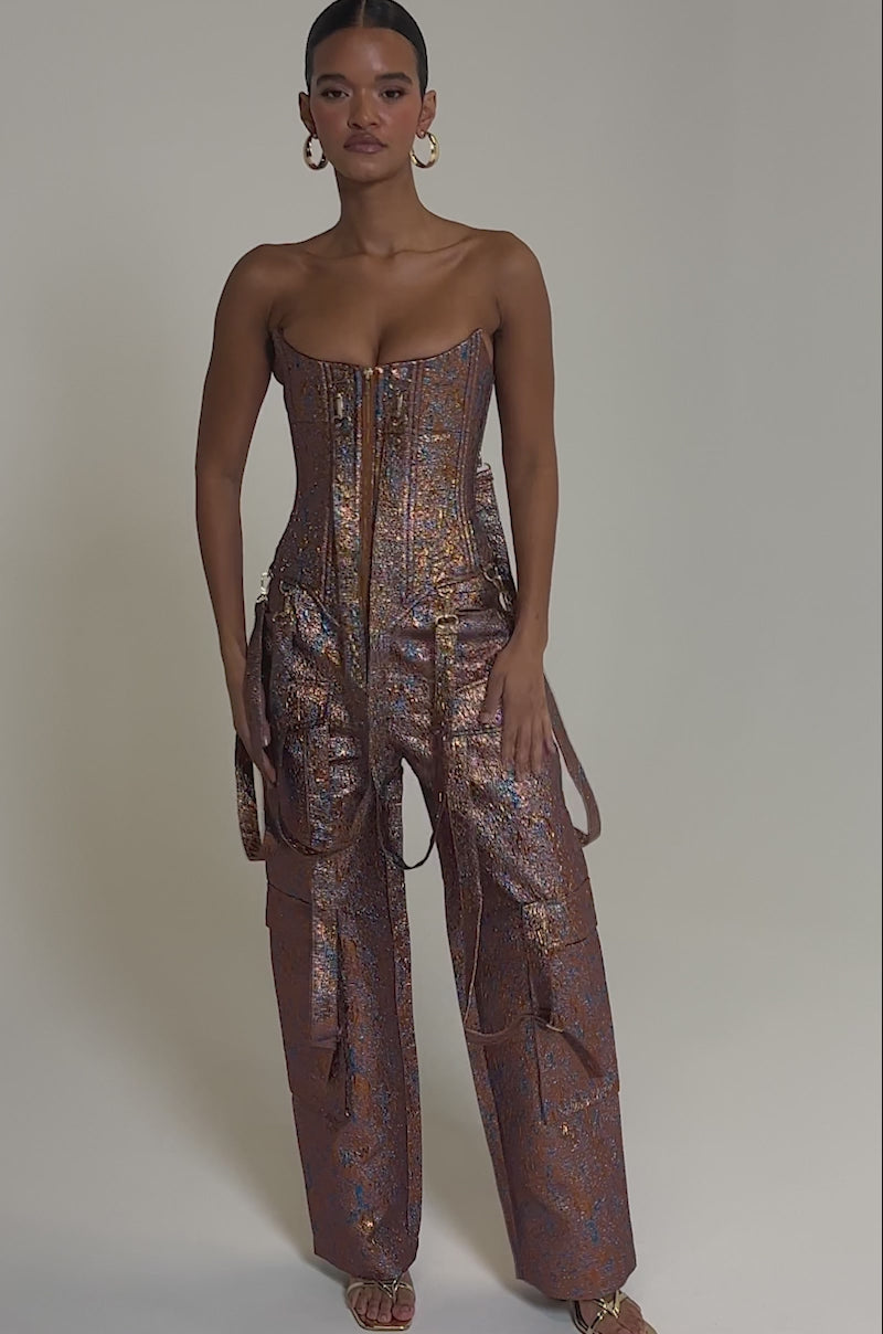 Video of woman modeling the CHECK IT OUT BROCADE BRONZE TROUSER, styled with a fitted strapless metallic top, wide-leg cargo details, slicked-back hair, gold hoop earrings, and strappy gold heels.