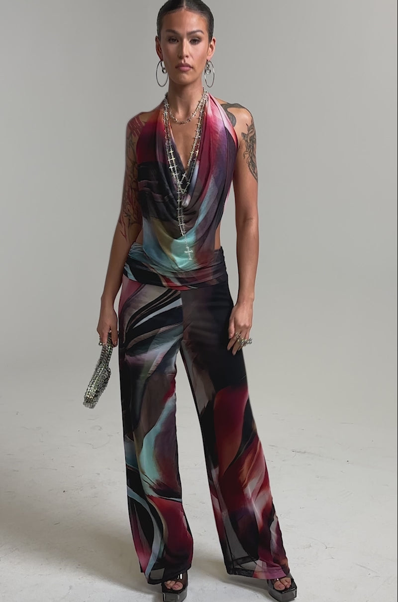 Video of woman modeling the MAIN CHARACTER ENERGY COWL NECK JUMPSUIT with wide-leg pants, accessorized with hoop earrings, layered necklaces, a chic handbag, and open-toe heels; her hair is slicked back for a stylish finish.