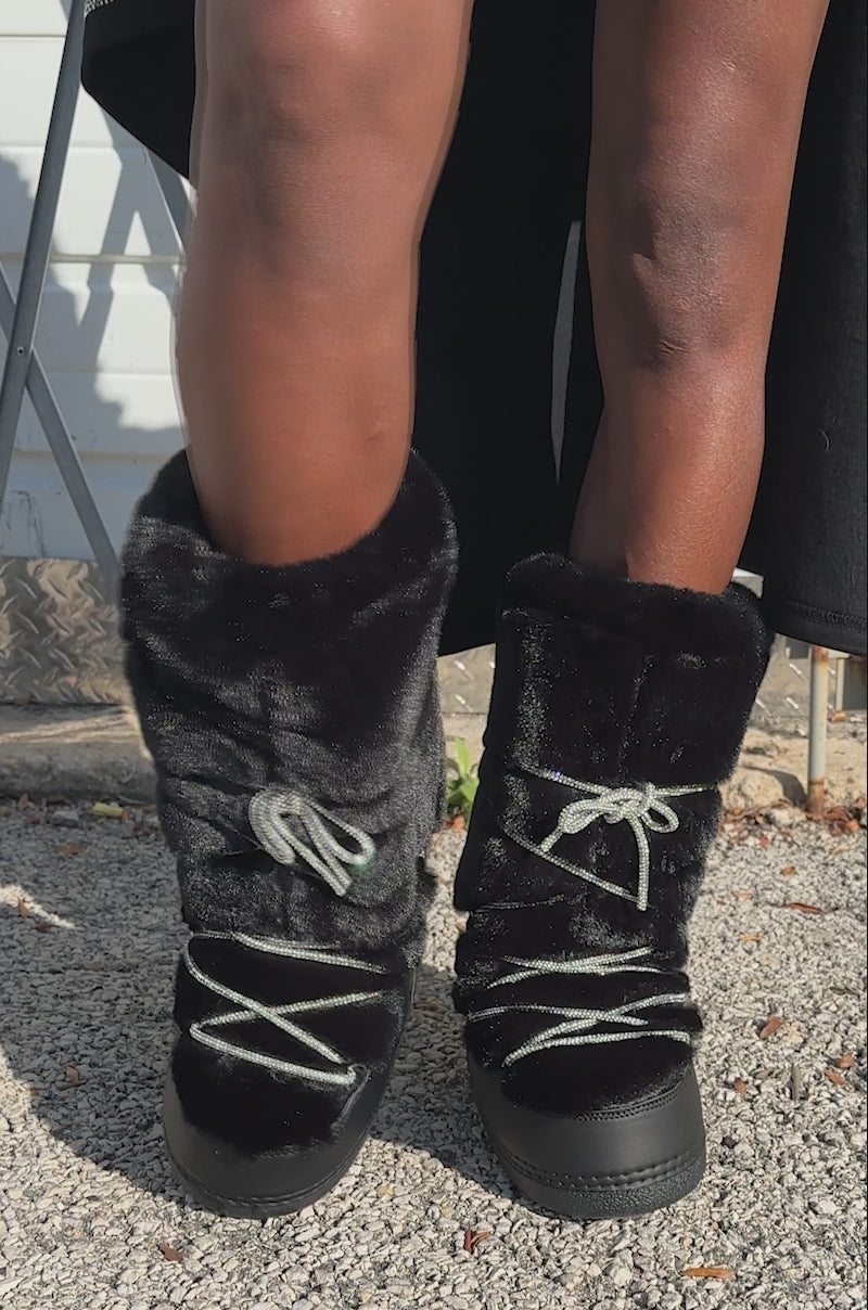 A video of a person wearing the cozy AZALEA WANG KARMELA BLACK FUR MOON BOOTS with silver laces. Only their legs and feet in the boots are visible.