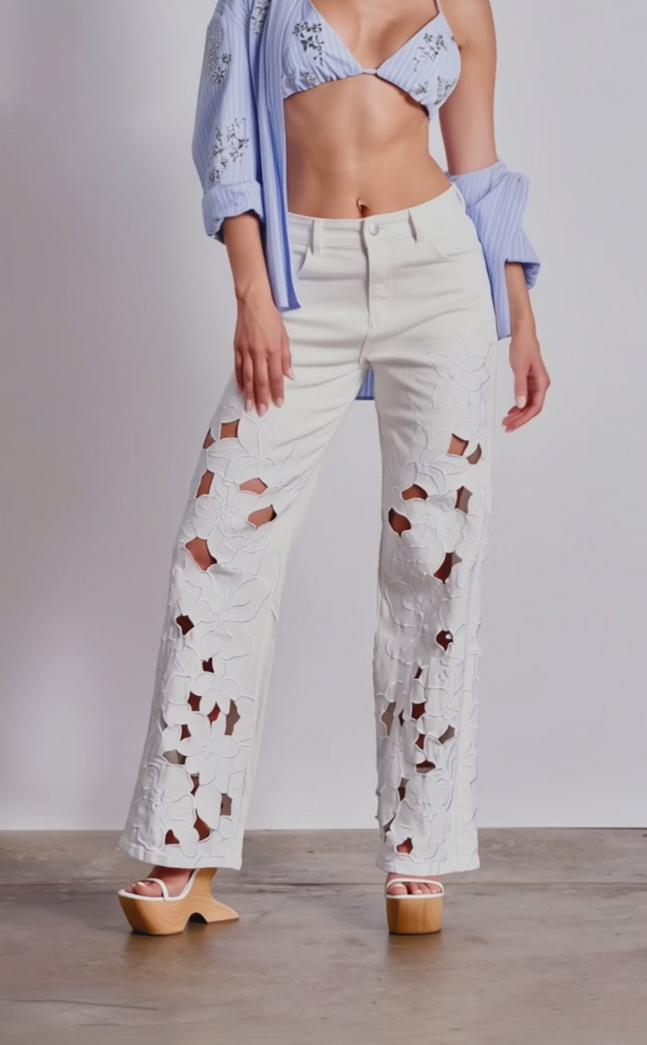 A video of a model wearing the LOVELY DAY FLORAL RELAXED DENIM, featuring white wide-leg jeans with large floral embroidery, styled with platform sandals.