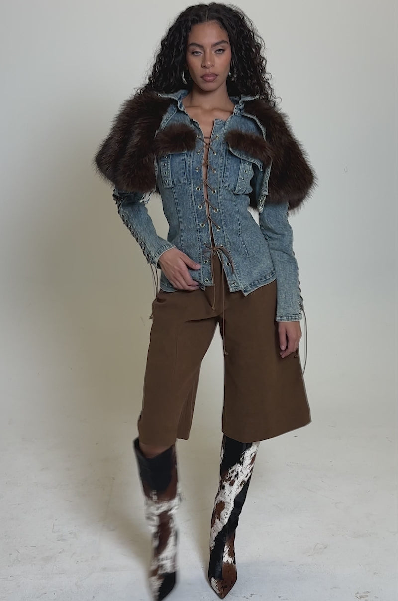 Video of woman modeling the KNOW IT SUEDE JORTS, a cropped denim jacket with lace-up sleeves, and knee-high black, white, and brown cowhide boots 