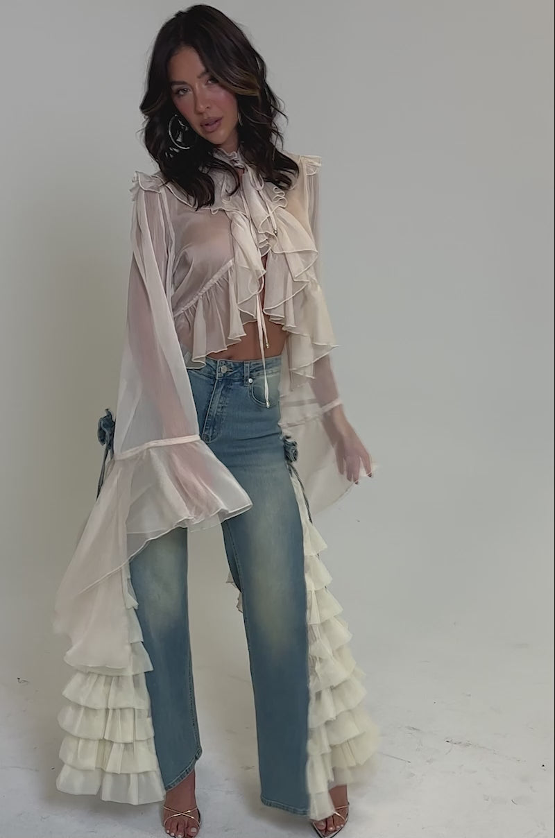Video of woman modeling the RUFFLE CITY STRAIGHT LEG DENIM with cream ruffled tulle sides, styled with a sheer flowy blouse and strappy high-heeled sandals.