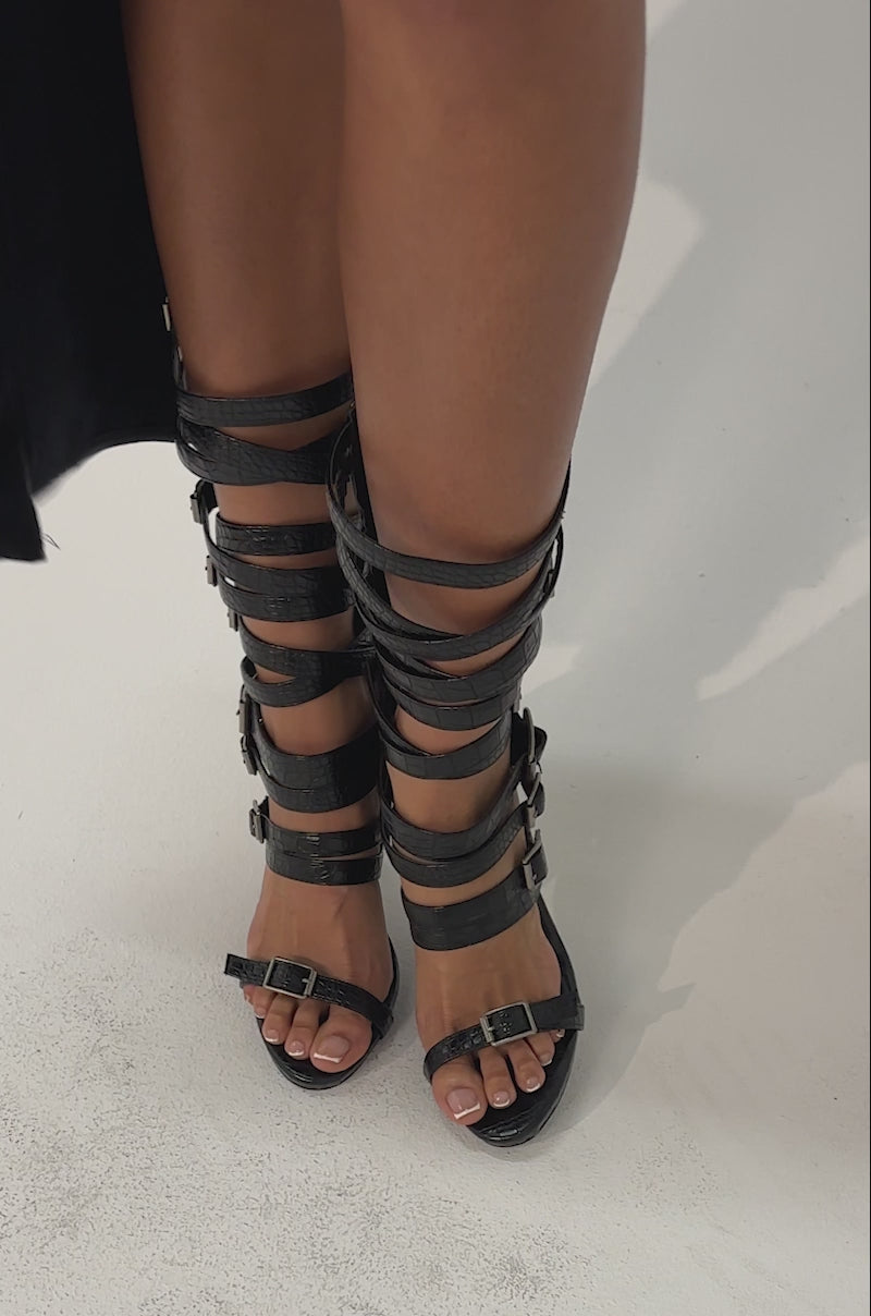 Video of woman modeling the AZALEA WANG HITCH BLACK CROC HARDWARE EMBELLISHED STILETTO SANDAL with multiple buckles against a neutral background.