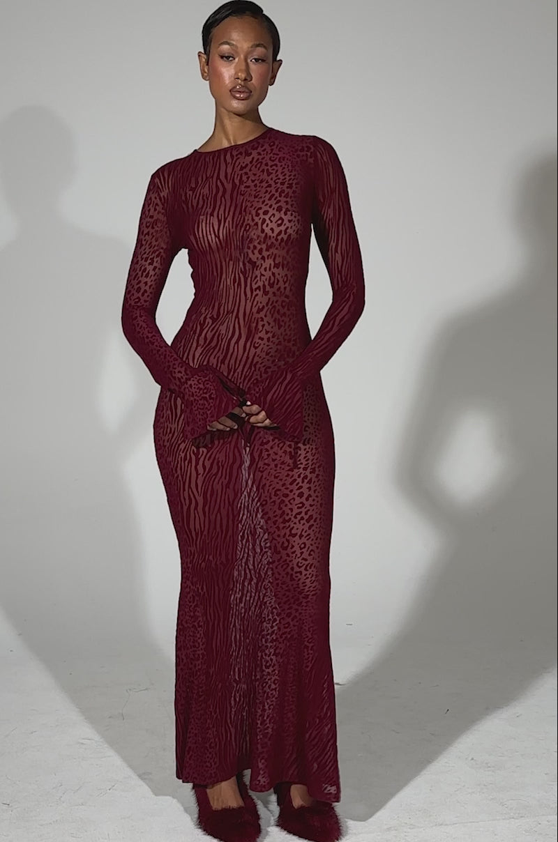 A video of a woman posing in the MY GOOD SIDE Leopard Mesh Maxi Dress in burgundy, featuring long sleeves and an animal print burnout pattern, against a plain light gray background.