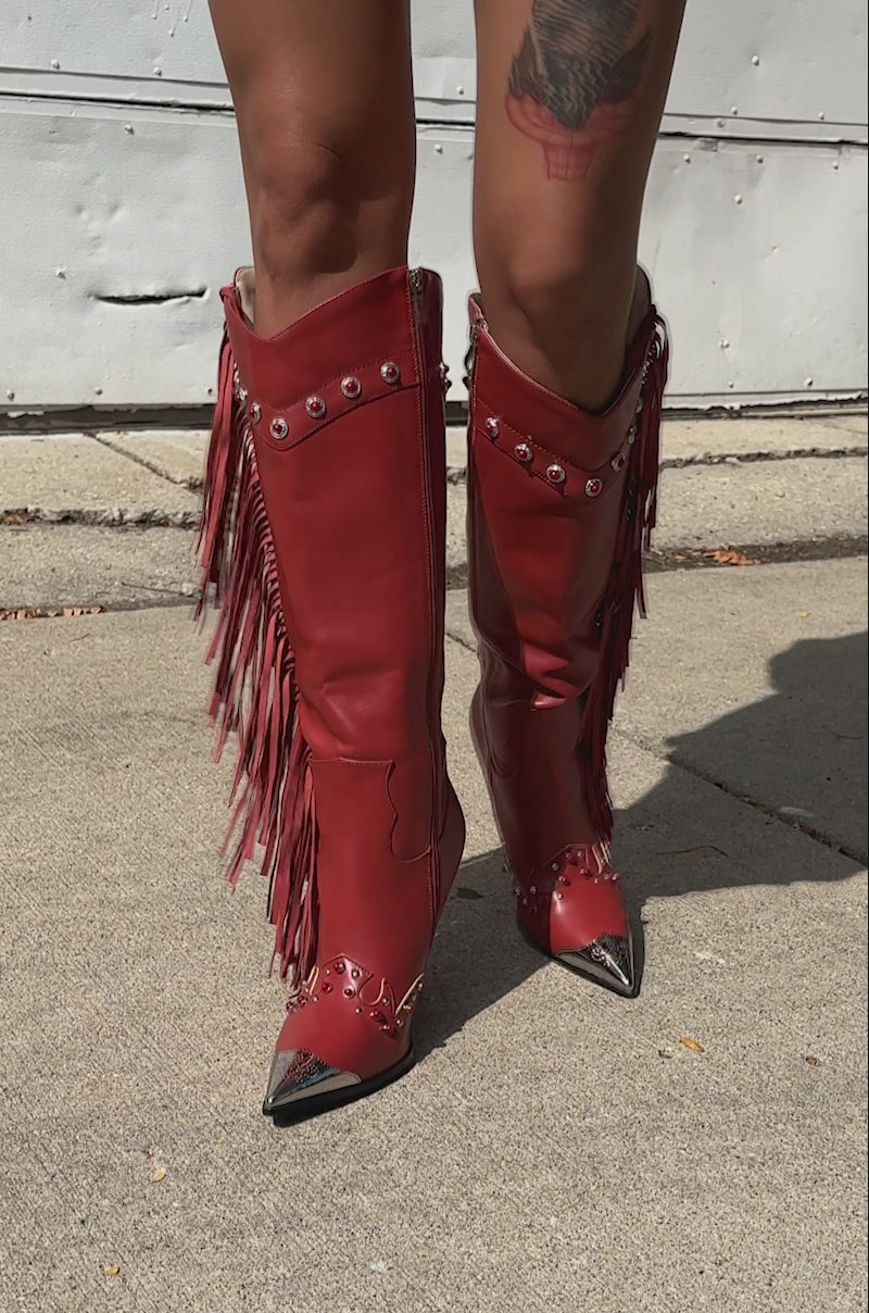 A video of a person in a white skirt, blue denim jacket, and AZALEA WANG PELAGIANA RED WESTERN POINTED TOE STILETTO BOOTS with silver accents stands on the sidewalk. A tattoo is visible on their upper leg.
