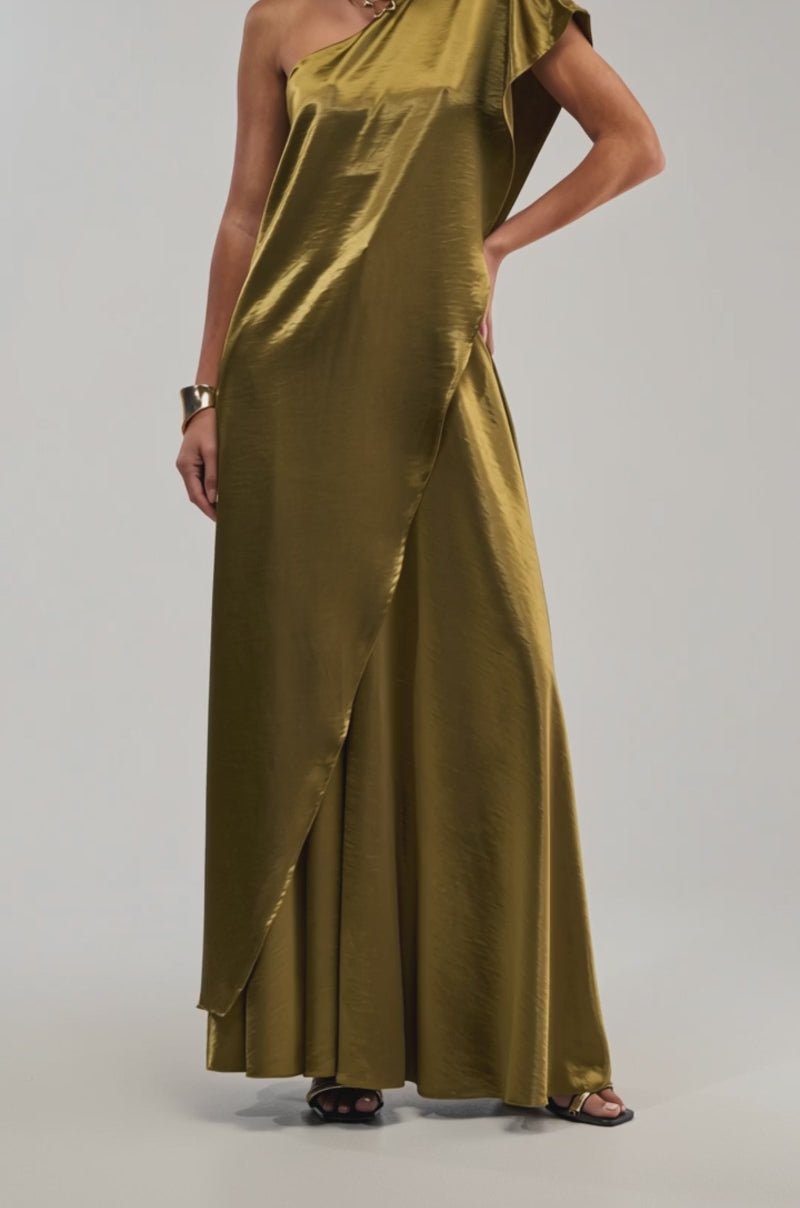 A video of a woman wearing the TRUE GODDESS ONE-SHOULDER TOP in shiny olive satin, styled as a floor-length gown with an asymmetrical sleeve. 