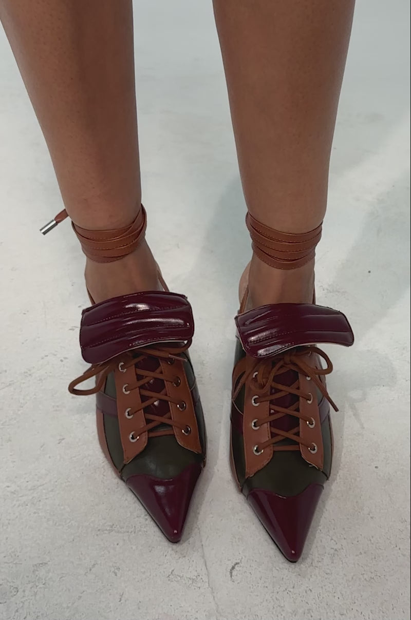 A video of a model wearing the AZALEA WANG AMBRE OLIVE COLORBLOCK MULTI MULE LACE UP STILETTO PUMP. It is a high-heeled, pointed-toe shoe with burgundy, olive green, and tan color blocks, padded tongue, and brown leather wrap-around ankle laces.