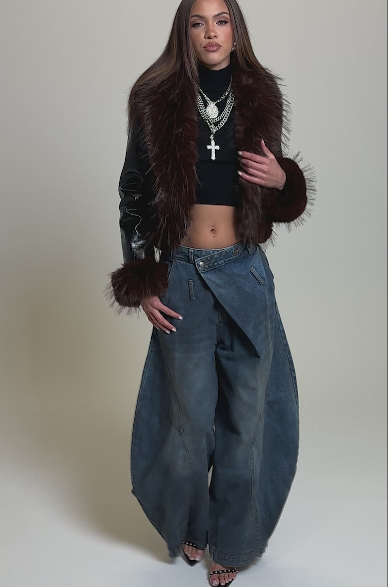 Video of woman modeling the LUNNA FUR TRIM MOTO IN BLACK CROC, layered over a black top and paired with high-waisted, draped blue jeans against a plain light background.