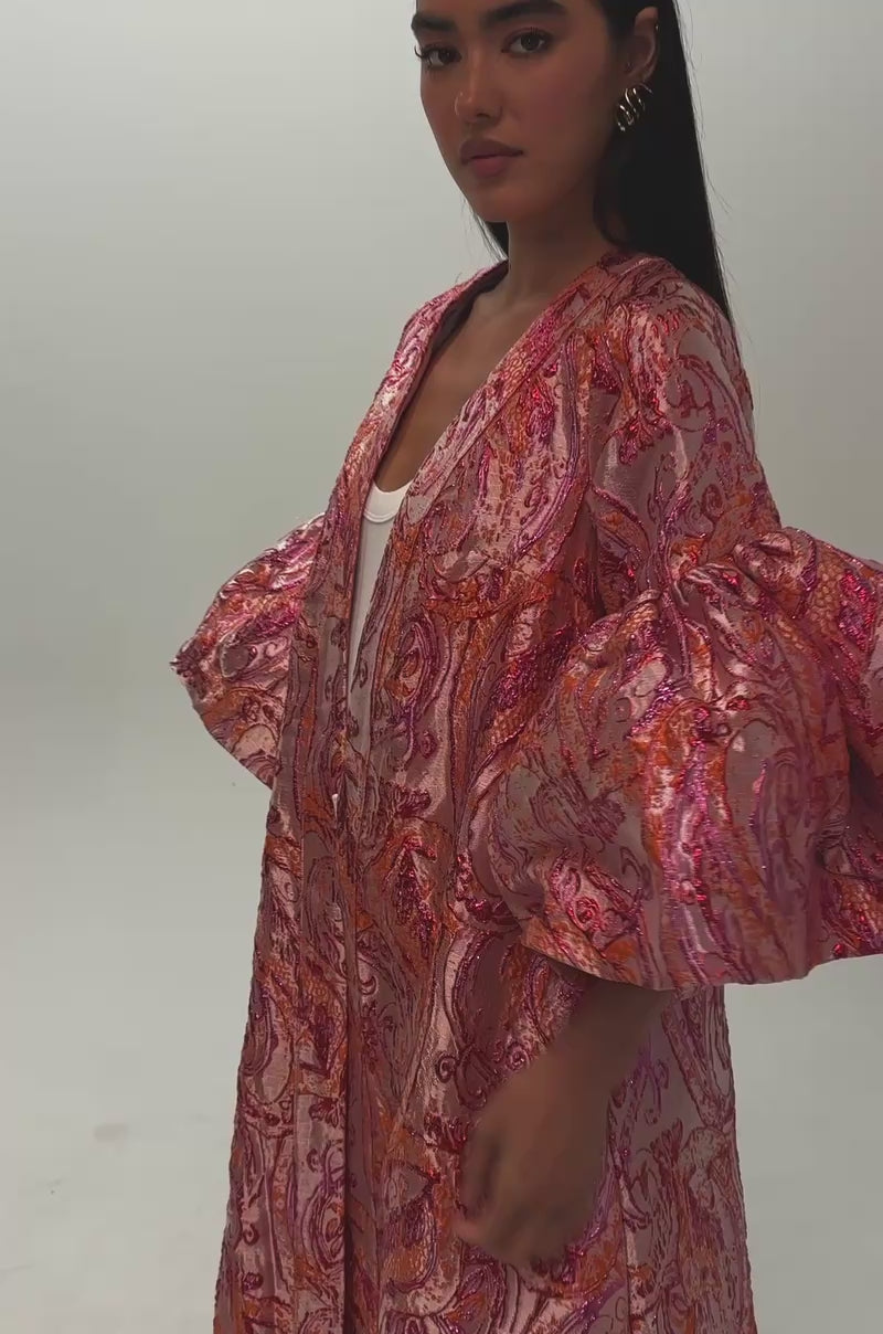 Video of a woman modeling the PINK SORBET BROCADE DUSTER—a vibrant hot pink and orange outerwear piece with a flowing, patterned design and puffy sleeves.