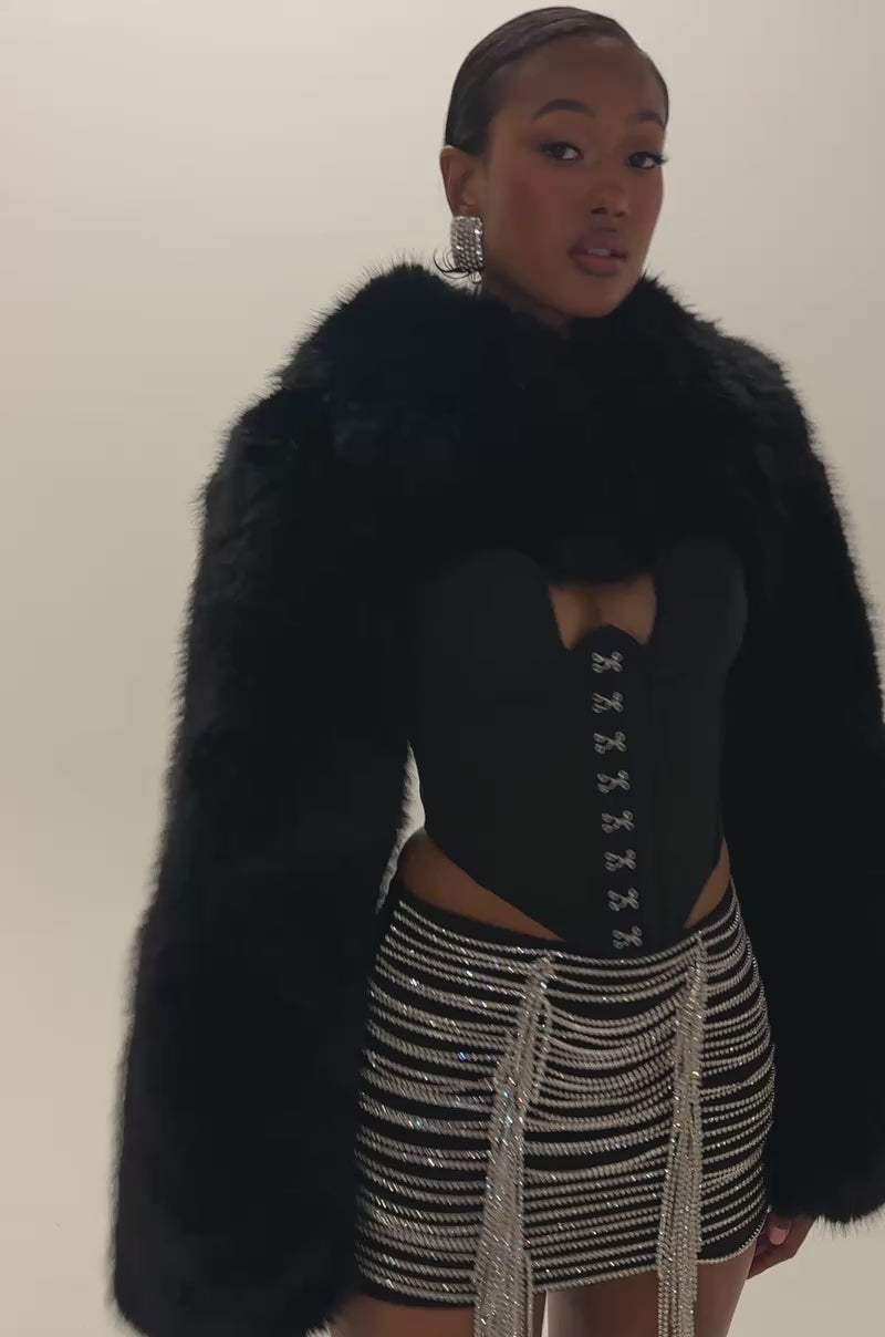 Video of a woman modeling the RHINESTONE LOVER MINI SKIRT—a black bodycon mini skirt embellished with draped chains and silver beading reminiscent of rhinestone fringe.