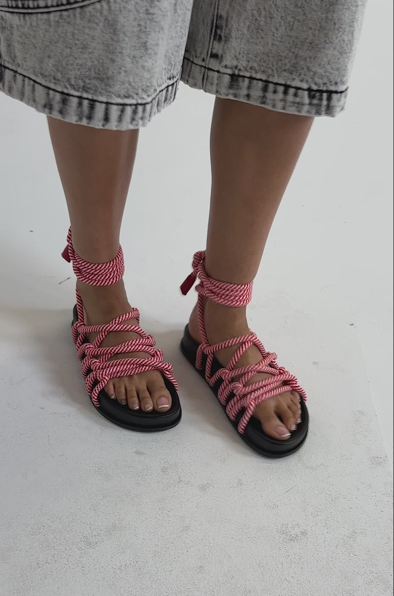 A video of a person wearing a light gray, knee-length denim shorts and the AZALEA WANG EINER RED ROPE FLATFORM SANDAL with red and white rope laces.