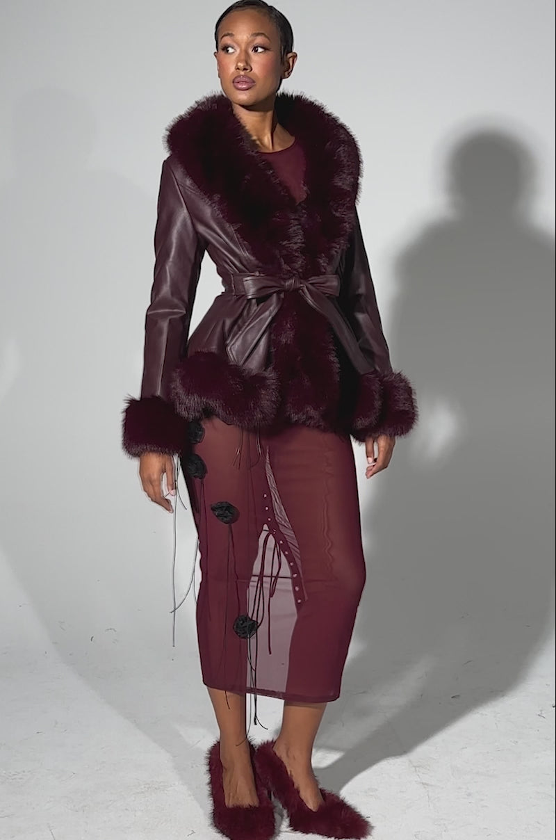 A video of a woman modeling the KENZY FUR TRIM MOTO IN BURGUNDY—an elegant deep burgundy moto jacket with fur collar and cuffs—over a matching floral dress and fluffy slippers against a plain gray background.