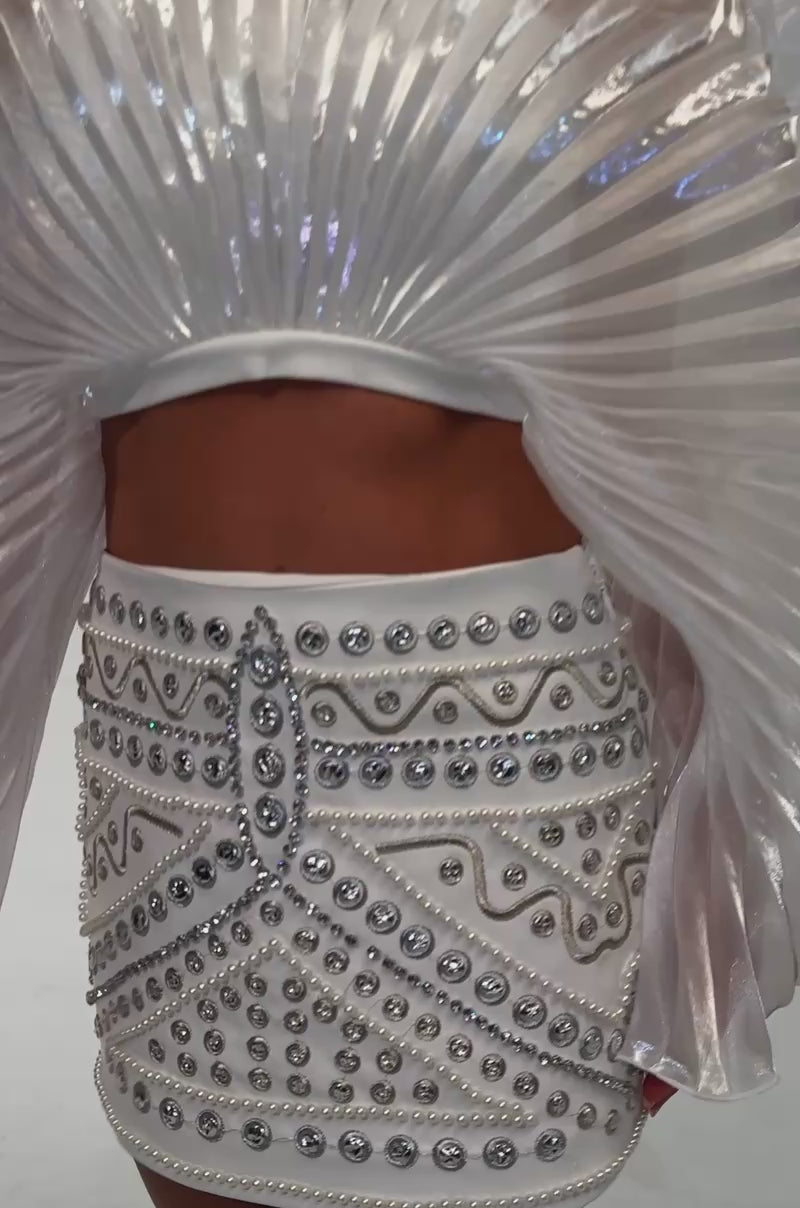 A video of a model wearing the GLAM GIRL MINI SKIRT, styled as a short white mini adorned with intricate patterns of silver and gold studs and pearls. 