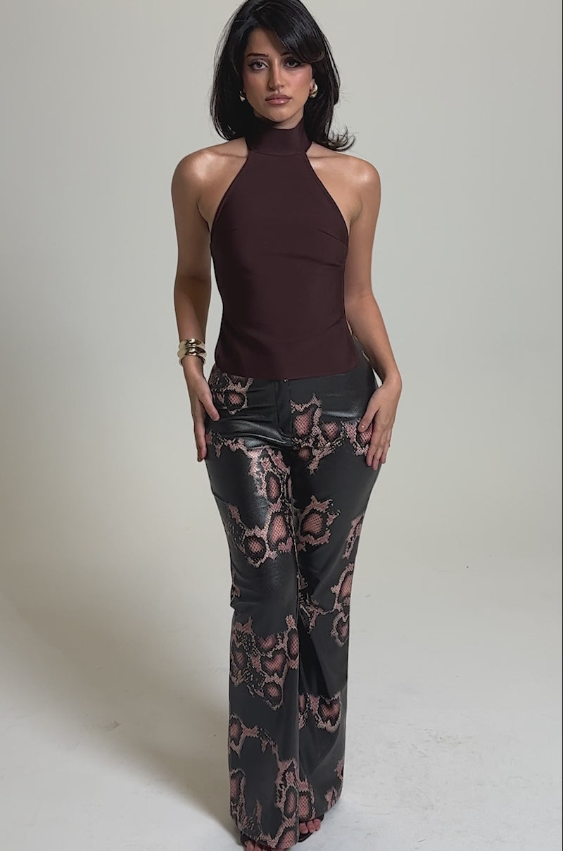 A video of a woman in the TRY ME BANDAGE BLOUSE, a sleeveless maroon halter top featuring an open-back detail, paired with high-waisted black pants with a pink and brown snakeskin pattern.
