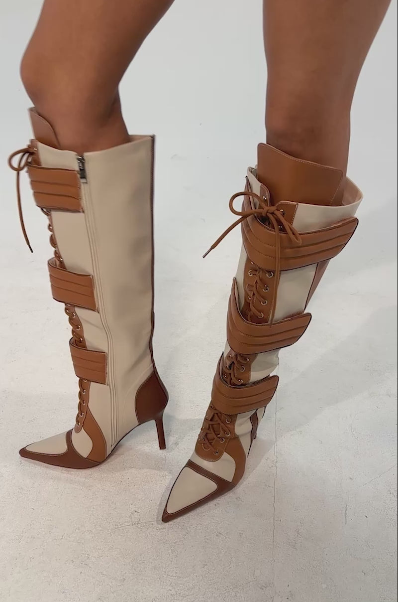 Video of woman modeling the AZALEA WANG SCHUMACHER TAN STILETTO BOOT featuring tan and cream knee-high style, pointed toes, high heels, lace-up fronts, and wide buckle straps
