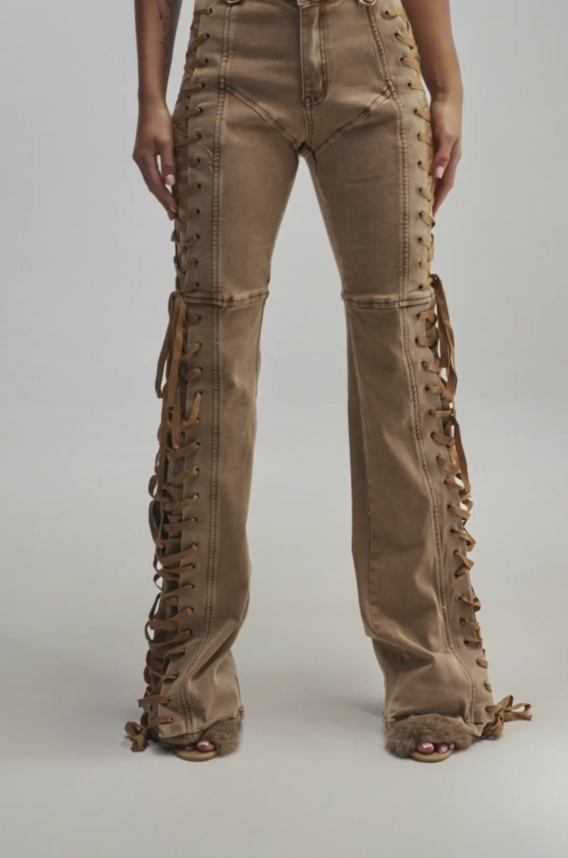 Video of a woman modeling the RIDE THAT WAVE LACE UP DENIM, this look features high-waisted brown denim pants with flared legs, eye-catching side laces, and visible stitching.