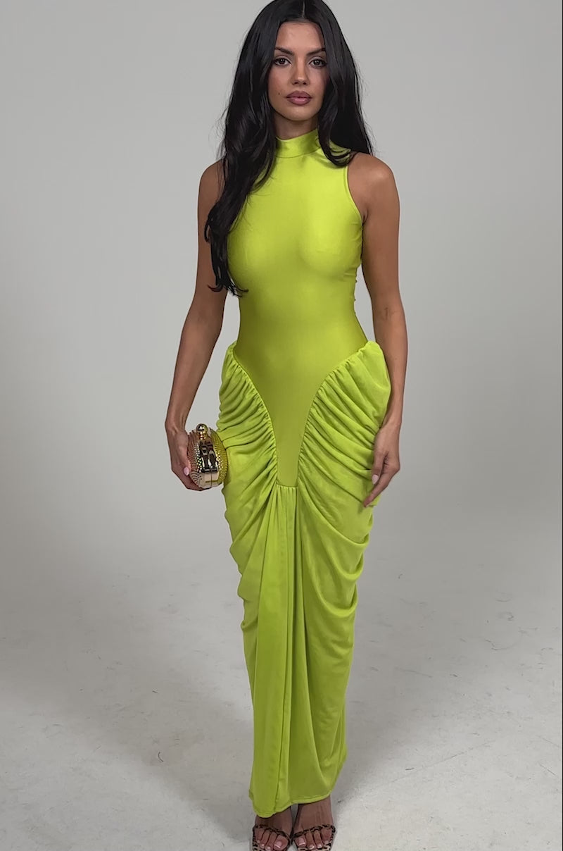 Video of woman modeling the SECOND DATE BODYCON SHINE MAXI DRESS IN CHARTREUSE, a sleeveless ruched maxi with high neck, paired with open-toe heels. 