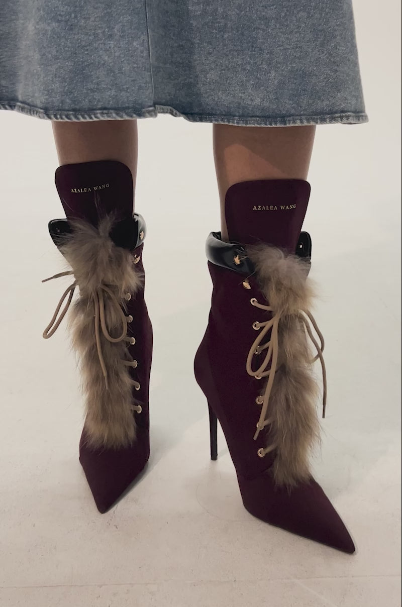 Video of woman modeling the AKIRA GOLD NYMERA Burgundy Stiletto Bootie with fur, featuring gold eyelets, pointed toes, and branded tongue.