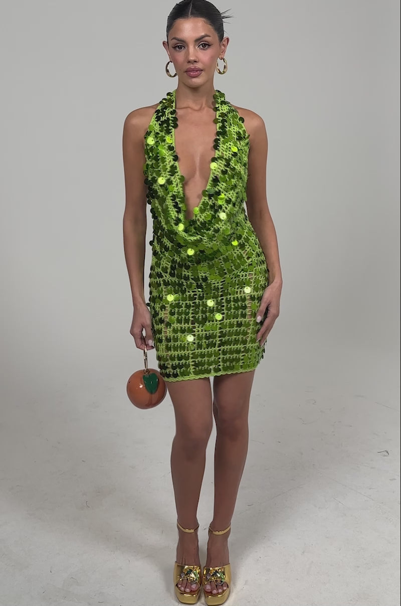 Video of woman modeling the ARIEL SEQUIN CROCHET MINI DRESS IN GREEN. She wears strappy gold shoes, radiating party-ready glamour against a plain light background.