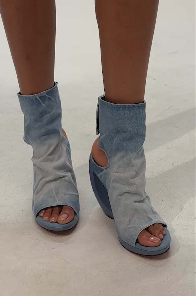 Video of woman modeling the AZALEA WANG CIRCOS LIGHT DENIM WEDGE BOOTIE, a pair of open-toe booties crafted in washed denim with distinctive curved blue wedge heels. 