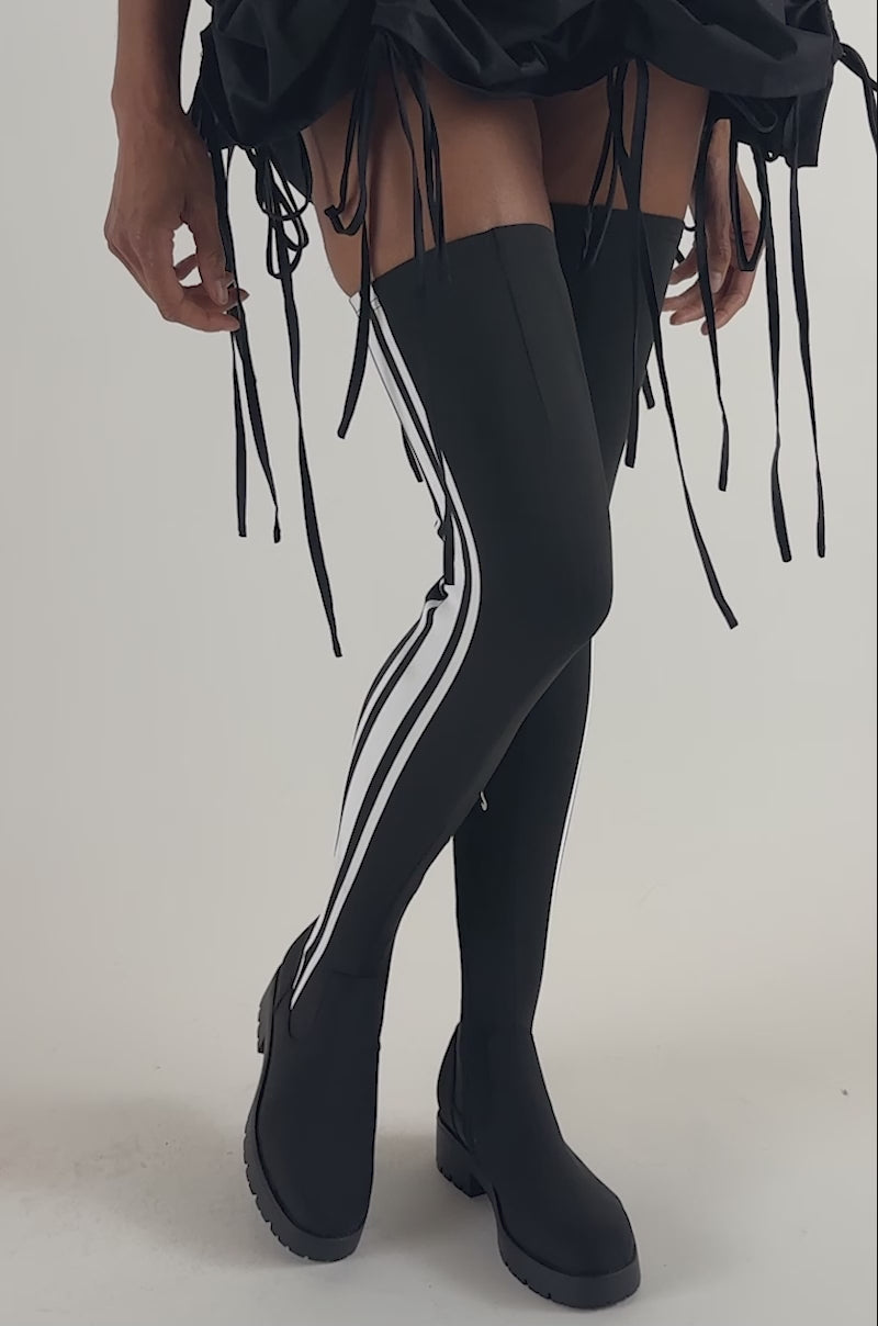 Video of a woman modeling the AKIRA GOLD DARBY BLACK FLAT STRETCH SPORTY BOOT.