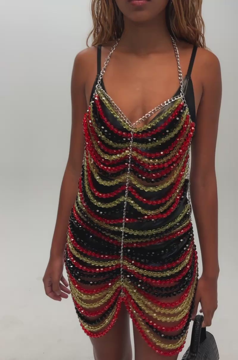 Video of a woman modeling the Carnivale Beaded Mini Dress in Green Multi—a beaded chain halter mini dress designed with layered green, yellow, and black beads.