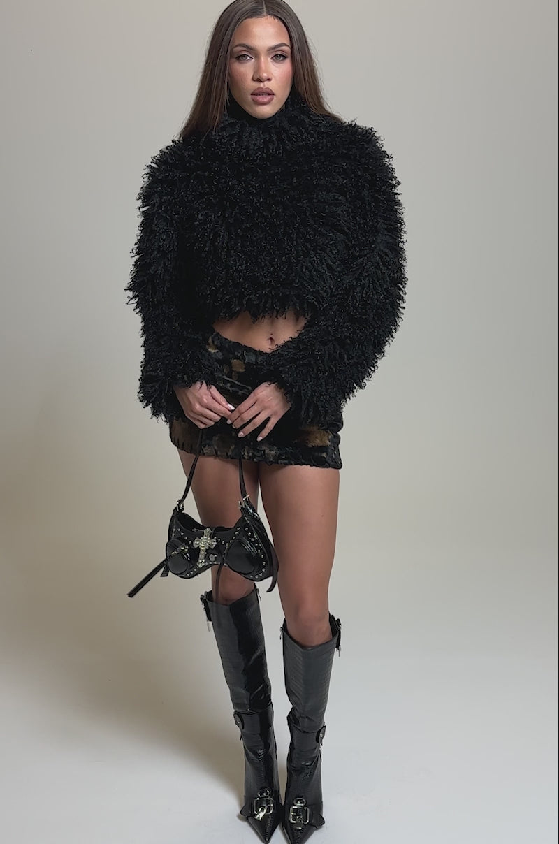 Video of woman modeling the COOL GIRL ALERT FUR TOP and a short brown and black tie-dye skirt, holding a small black purse against a plain light-colored background.