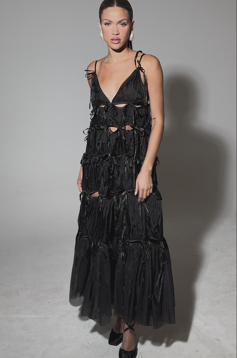 Video of woman modeling the COULDN'T BE ME IF YOU TRIED TIE MAXI DRESS IN BLACK—tiered, sheer tulle with ribbon details and spaghetti straps—paired with black lace-up shoes.