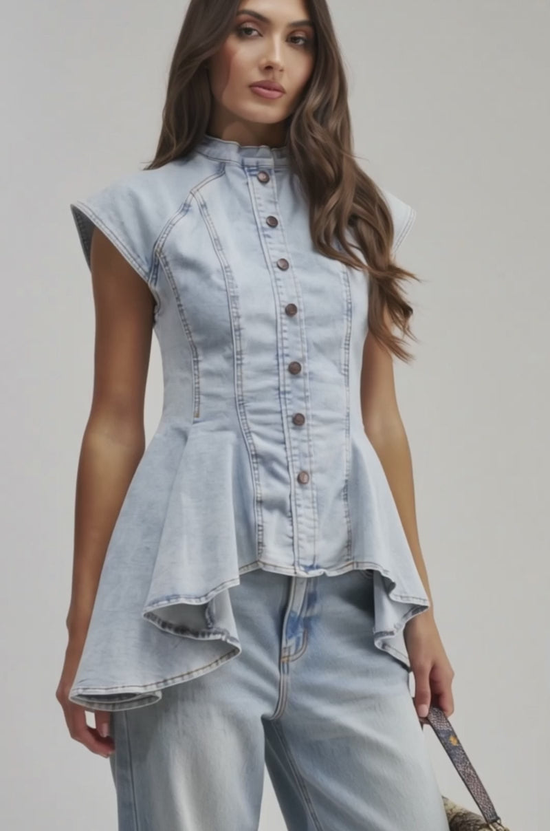 Video of a woman modeling the LUCY DENIM BLOUSE—a sleeveless, light blue button-down with a high collar and flared peplum hem.