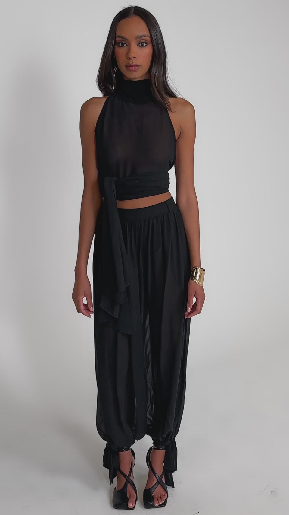 Video of woman modeling the TRENDY BALLON PANT tied at the ankles with a sheer black sleeveless high-neck top and black heeled sandals.