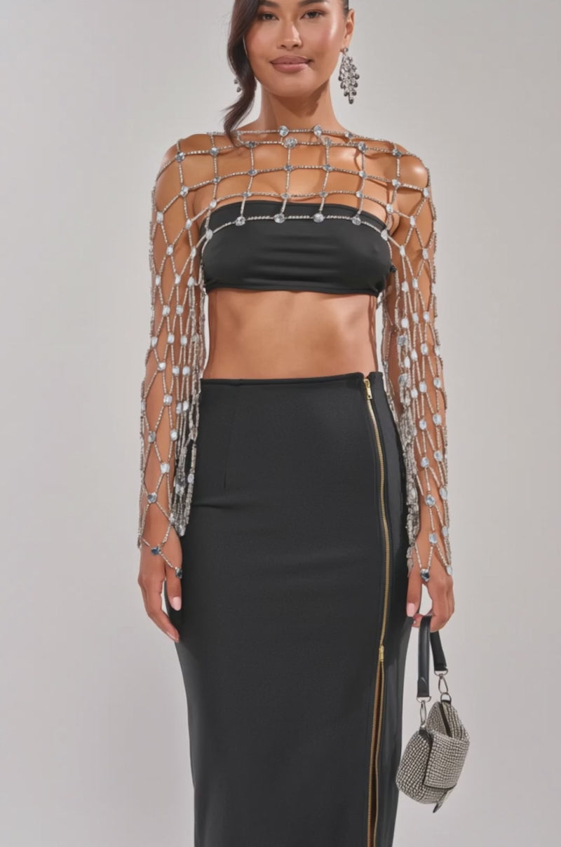Video of woman modeling the CHAINED TO YOU TOP, styled with a beaded netted cape, dangling earrings, and a sparkling small handbag, standing confidently against a plain background.