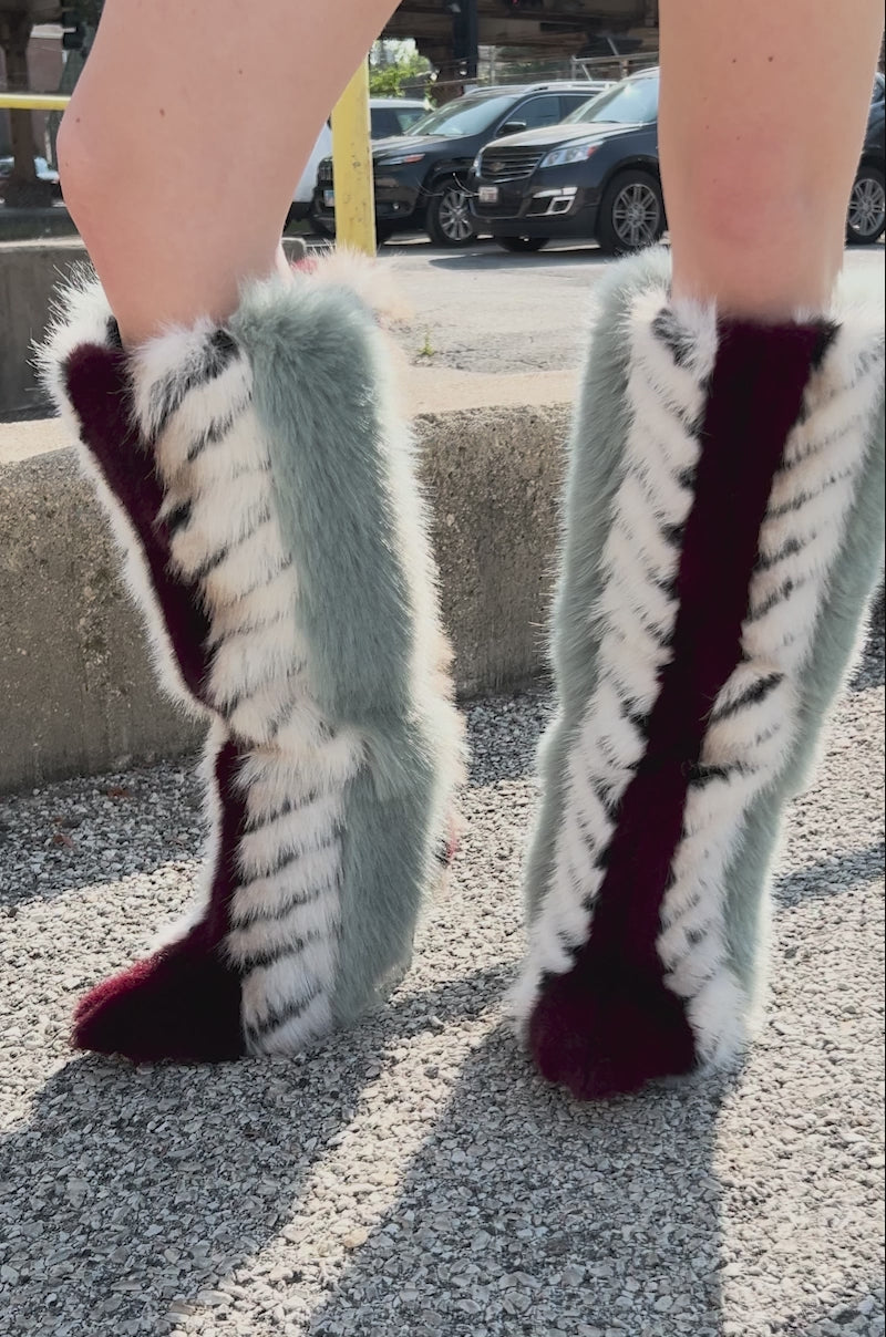 Video of person showing off the AZALEA WANG UPSELLA BLUE MULTI STILETTO BOOT. Featuring a knee-high length, pointed-toe faux fur boot in bold colors—white with black stripes, burgundy, and a striking vertical blue-green stripe.